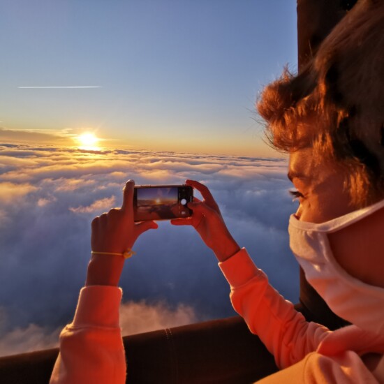 Une personne prend en photo le soleil au dessus des nuages
