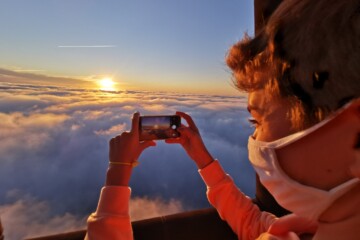 Une personne prend en photo le soleil au dessus des nuages