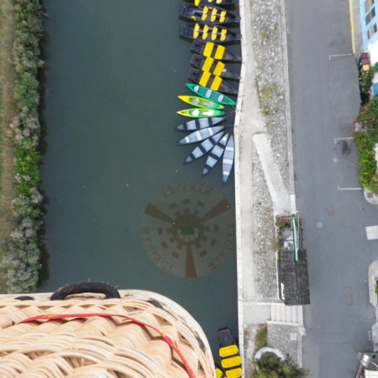 Montgolfière au-dessus d'un canal avec des barques colorées.