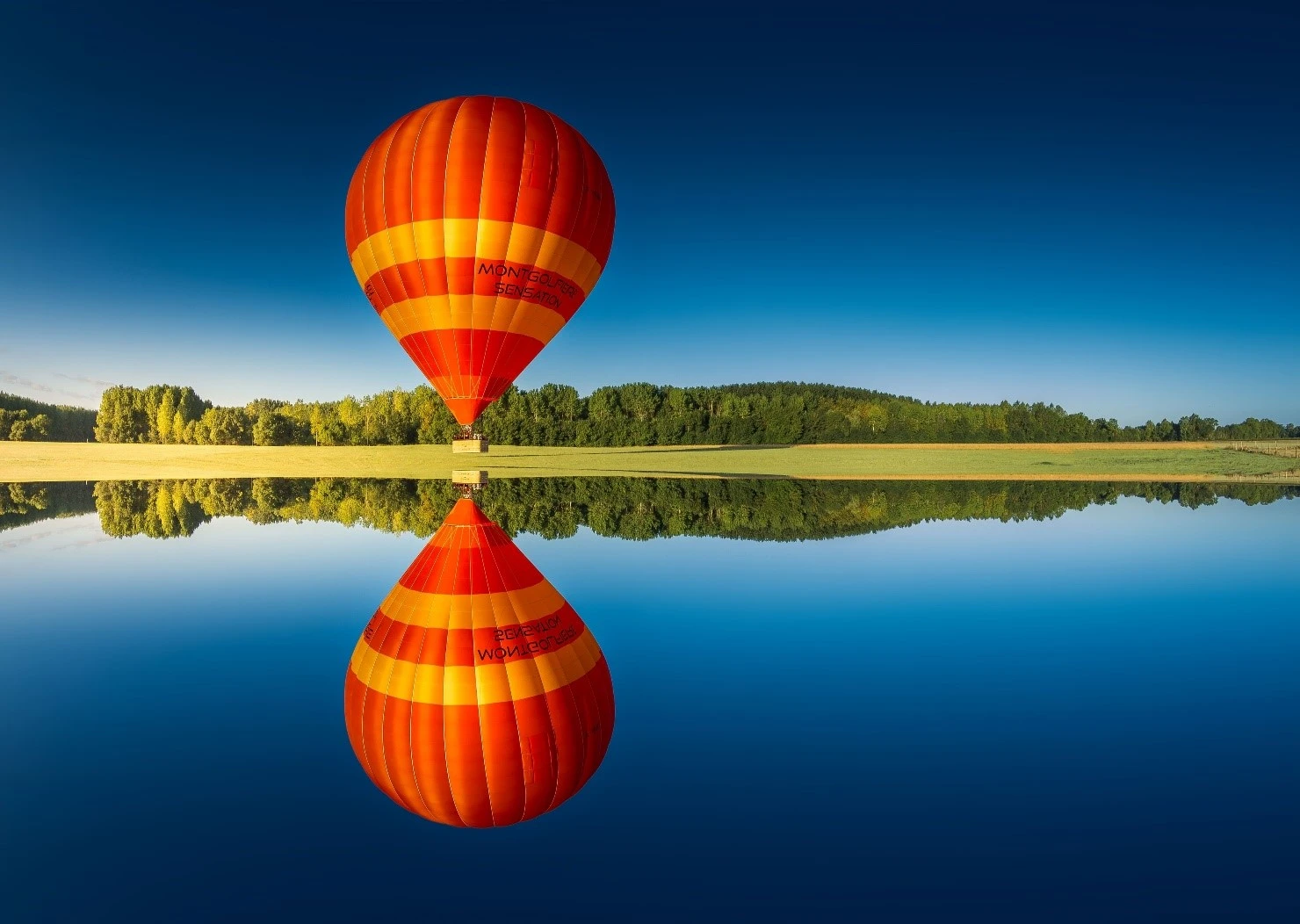 Montgolfière survolant un lac et se refletant dans l'eau.