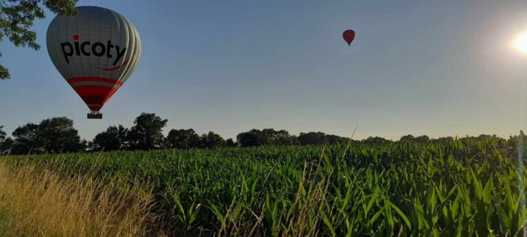 Deux montgolfière en vol au dessus d'un champs de maïs au printemps